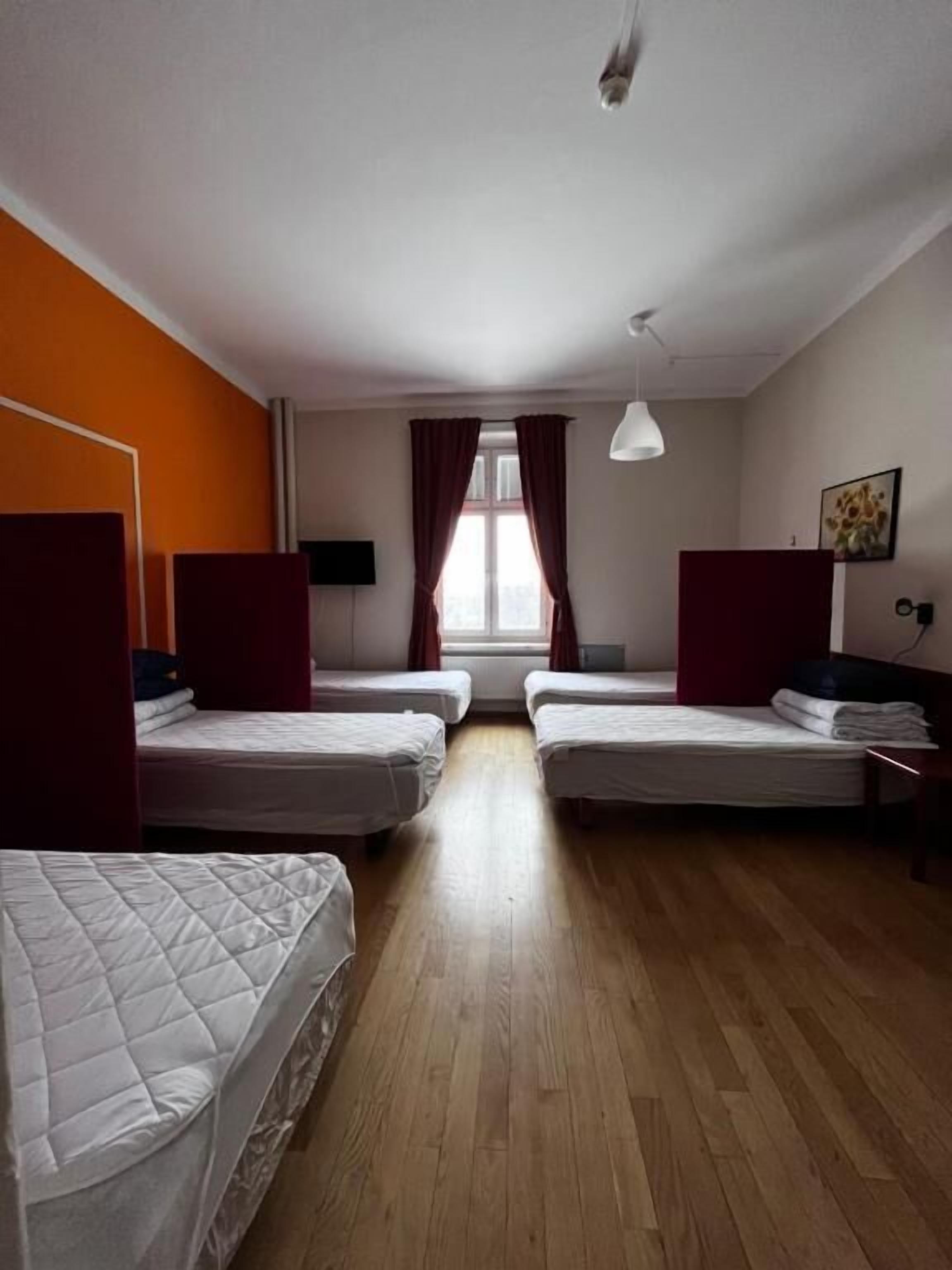 Habitación de hotel con dos camas individuales, piso de madera, ventana con cortinas, ventilador de techo y un cuadro en la pared.