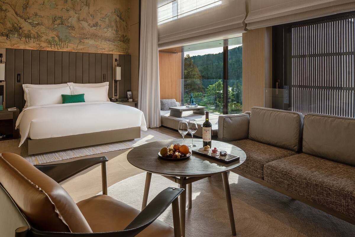 Ett modernt hotellrum med en stor säng, en soffa, ett matbord och utsikt över omgivningarna.