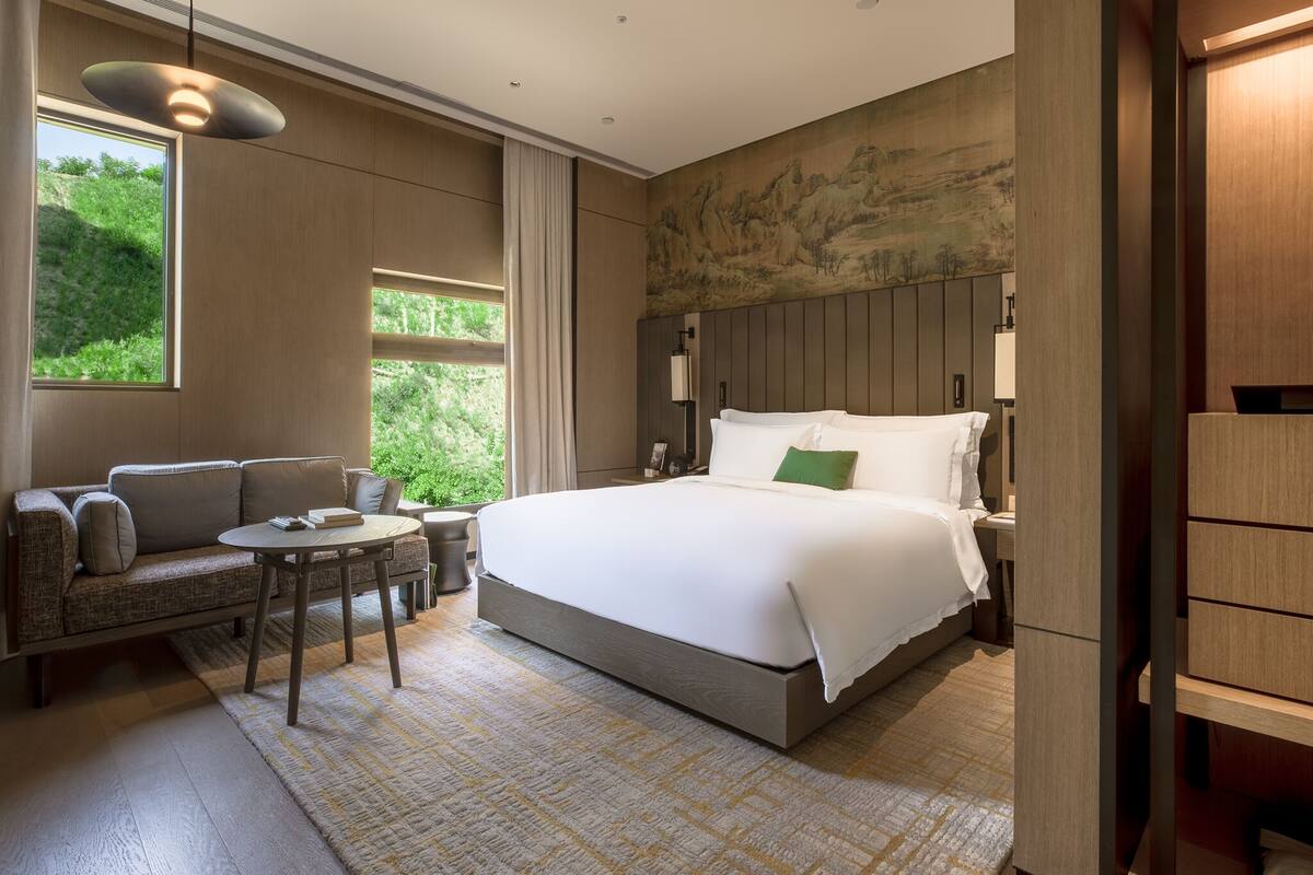 Ett modernt hotellrum med en stor säng, en soffa, ett litet bord och utsikt över grönområden genom fönstret.