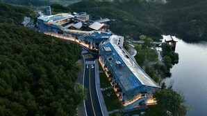 A modern hotel with a unique architectural design, situated by a lake surrounded by lush greenery. - Yanbai Villa, Beijing (Huairou)