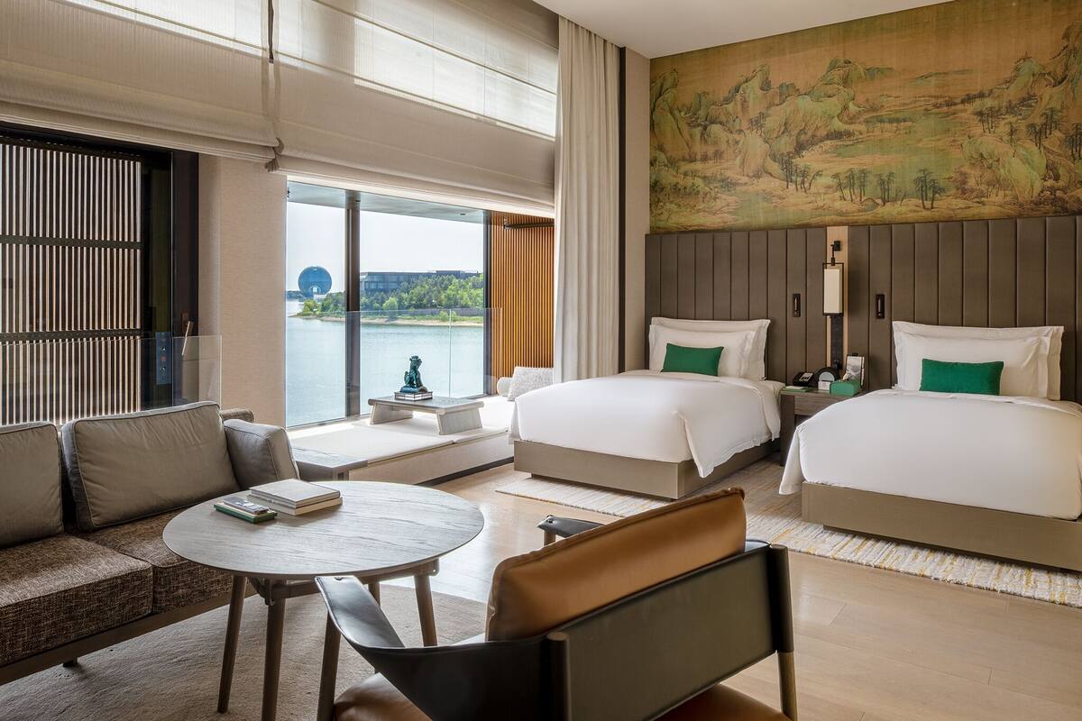 Ett hotellrum med två sängar, en soffa, ett bord och utsikt över en sjö eller ett annat vattendrag.