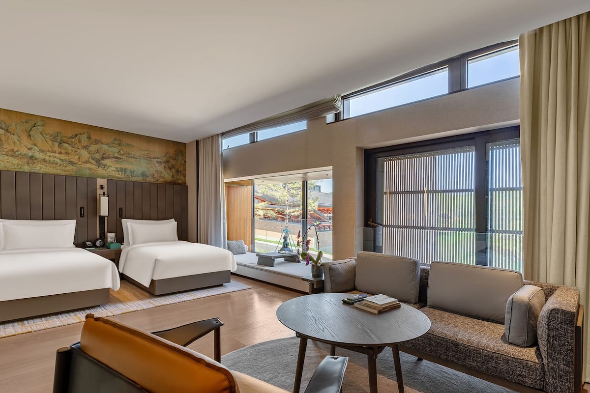 Ett hotellrum med två sängar, en soffa, ett soffbord och ett stort fönster med utsikt över omgivningarna.
