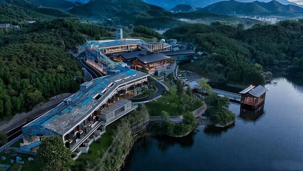 An aerial view of a hotel with multiple buildings, a swimming pool, and a dock extending into a lake, surrounded by forested hills. - Yanbai Villa, Beijing (Huairou)