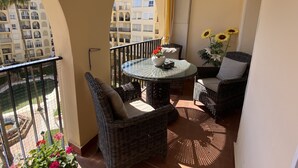 Ein Balkon mit Korbmöbeln, einem Glastisch und einer Vase mit Sonnenblumen.