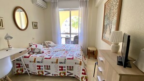Ein Schlafzimmer mit Bett, Schreibtisch, Stuhl, Lampe und einem Fenster mit Vorhängen.