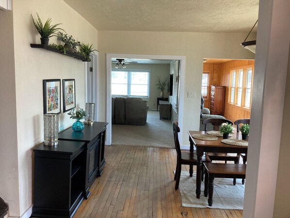 A spacious living area with a wooden floor, a dining table with chairs, a black entertainment unit, and a hallway leading to a kitchen area. - Charming Cecil Cottage Next To Landing! (Cecil)