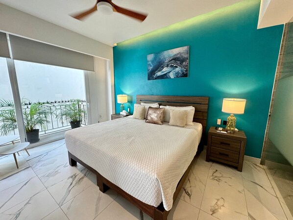 Un dormitorio con cama, mesitas de noche, ventilador de techo y vistas al balcón exterior.