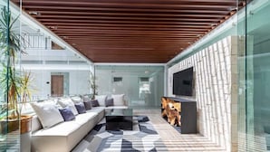 A modern living room with a sectional sofa, a coffee table, and a TV. There is a wooden ceiling and a stone wall with a fireplace.