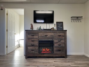 A living room with a fireplace, a television mounted on the wall, and a welcome sign.