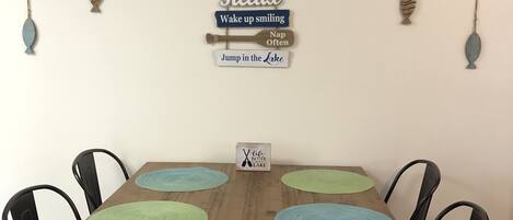 Une table à manger avec quatre chaises, une décoration murale en bois ornée de phrases motivantes et un petit panneau fixé au mur.