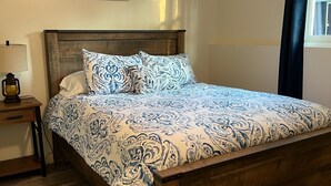 Une chambre à coucher avec un lit en bois, une literie à motifs, une table de chevet avec une lampe et un ventilateur de plafond.