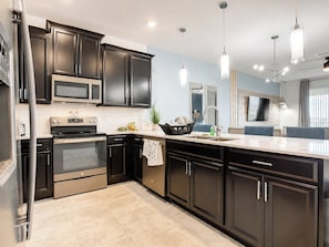 A modern kitchen with dark cabinetry, stainless steel appliances, and pendant lighting.