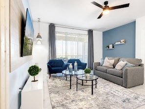 A modern living room with a sofa, armchairs, a coffee table, and a ceiling fan.