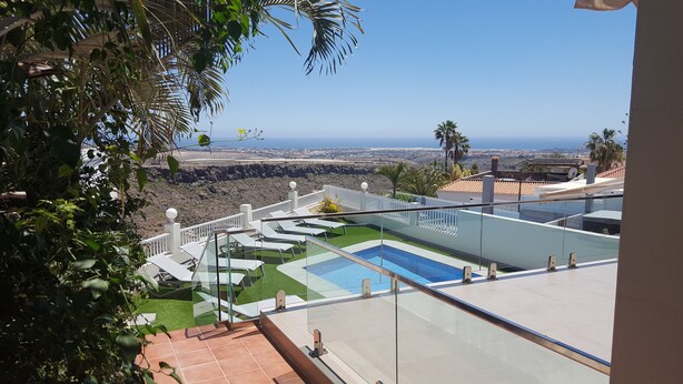 Piscina en la azotea con vista al océano, rodeada de barandillas blancas y palmeras.