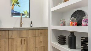 A modern kitchen with a wooden cabinet, a sink, and a window with a view of palm trees.