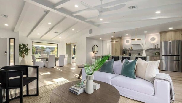 A modern living room with a white sofa, a round coffee table, and a black chair. There is a kitchen area with stainless steel appliances and a dining area with a white table and chairs. - The Kingsley|Custom|Heated Pool|Chef Kitchen|Chess (Scottsdale)