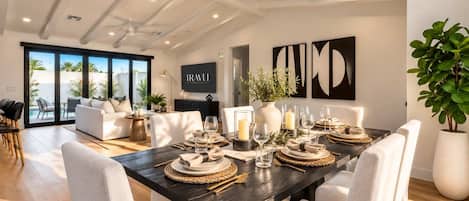 A dining area with a dark wooden table set for six, surrounded by white chairs.