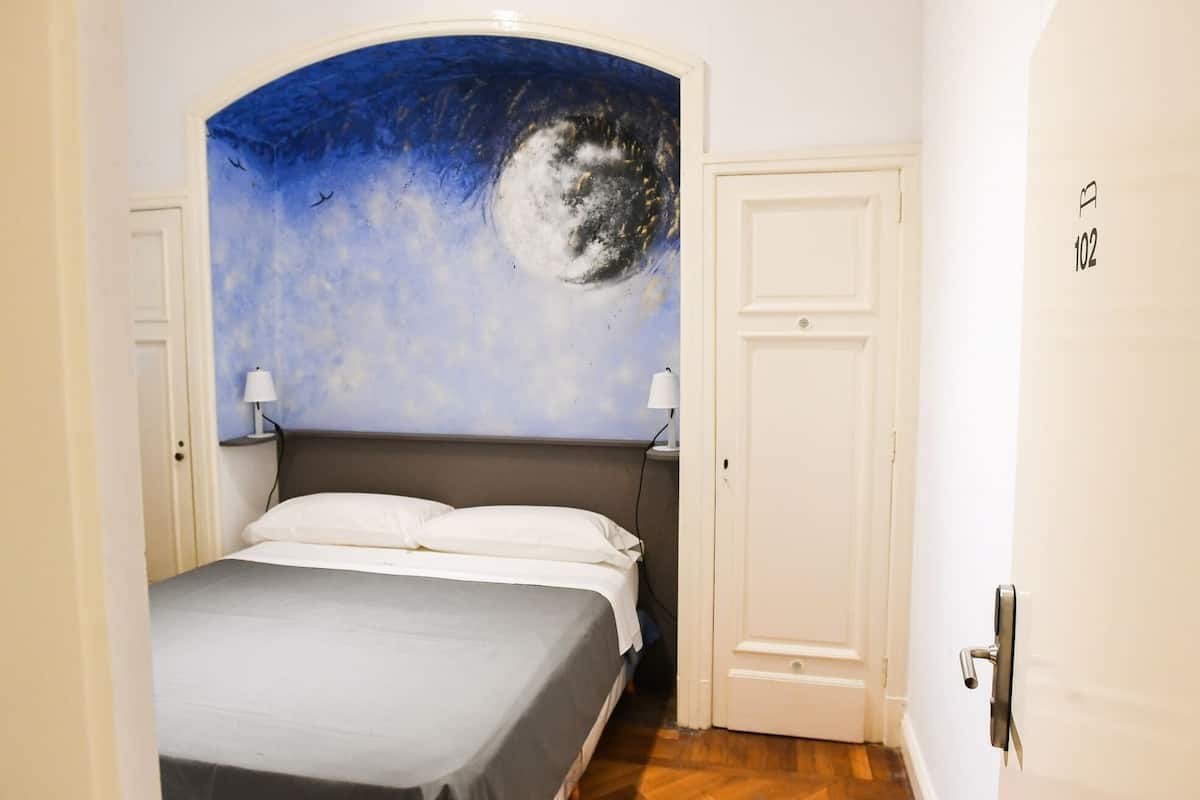 Ein Schlafzimmer mit einem Bett, zwei Nachttischlampen, einer Tür und einem Wandbild mit einem Mond.
