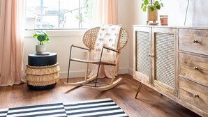 A room with a large window, a rocking chair, a wooden cabinet, and a striped rug.