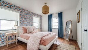 A bedroom with a bed, a bedside table, a mirror, and a window with curtains.