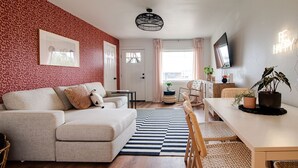 A living room with a sofa, a dining table, a TV, and a patterned wall.