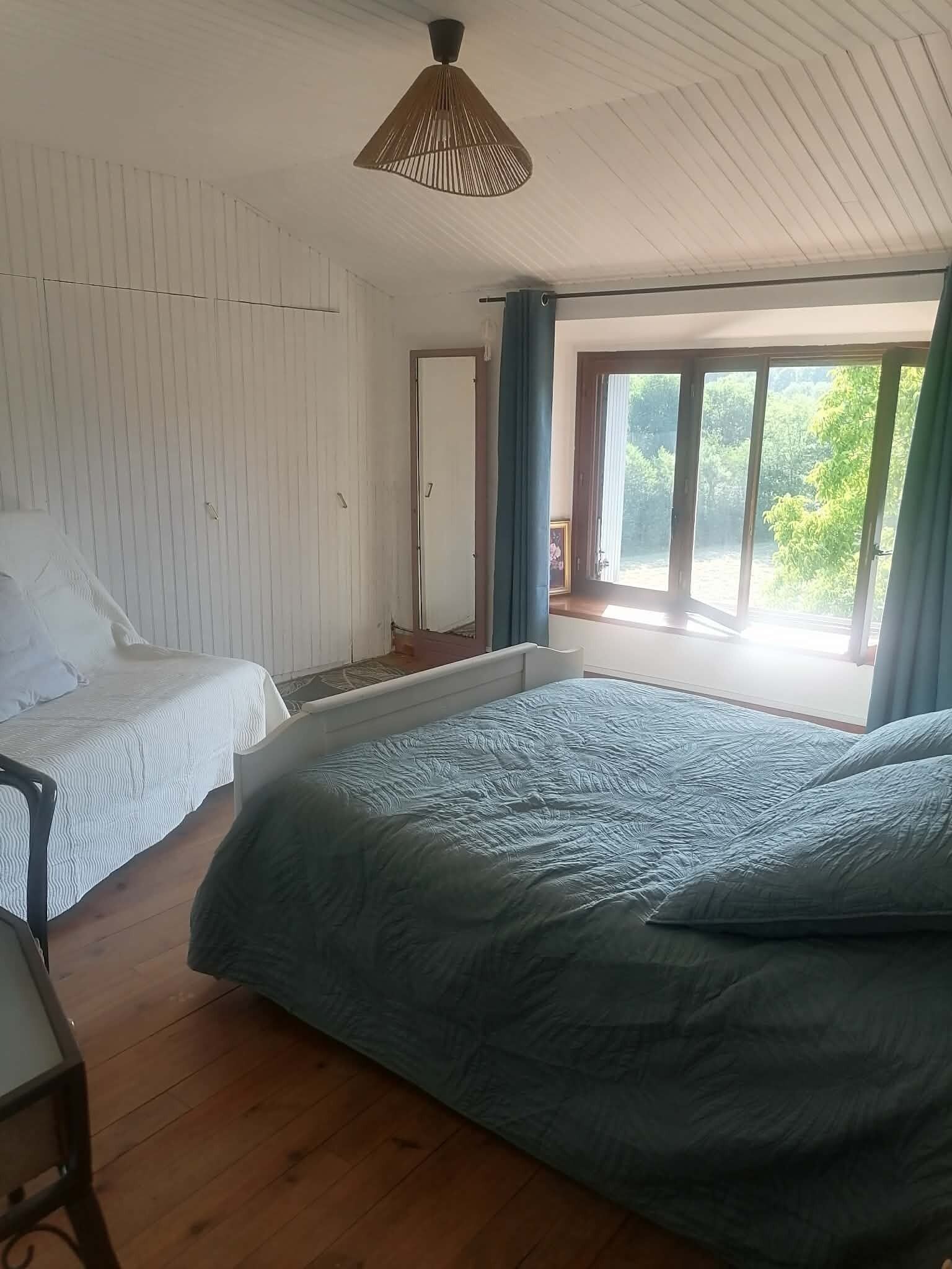 A bedroom with two beds, a wooden floor, a ceiling fan, and a window with curtains.