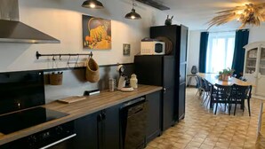 A modern kitchen with a black stove, microwave, and refrigerator. There is a wooden countertop, hanging pots, and a dining area with a table and chairs.