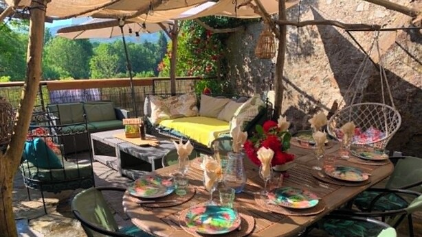 An outdoor patio with a dining table set for a meal, surrounded by chairs and a hanging chair.