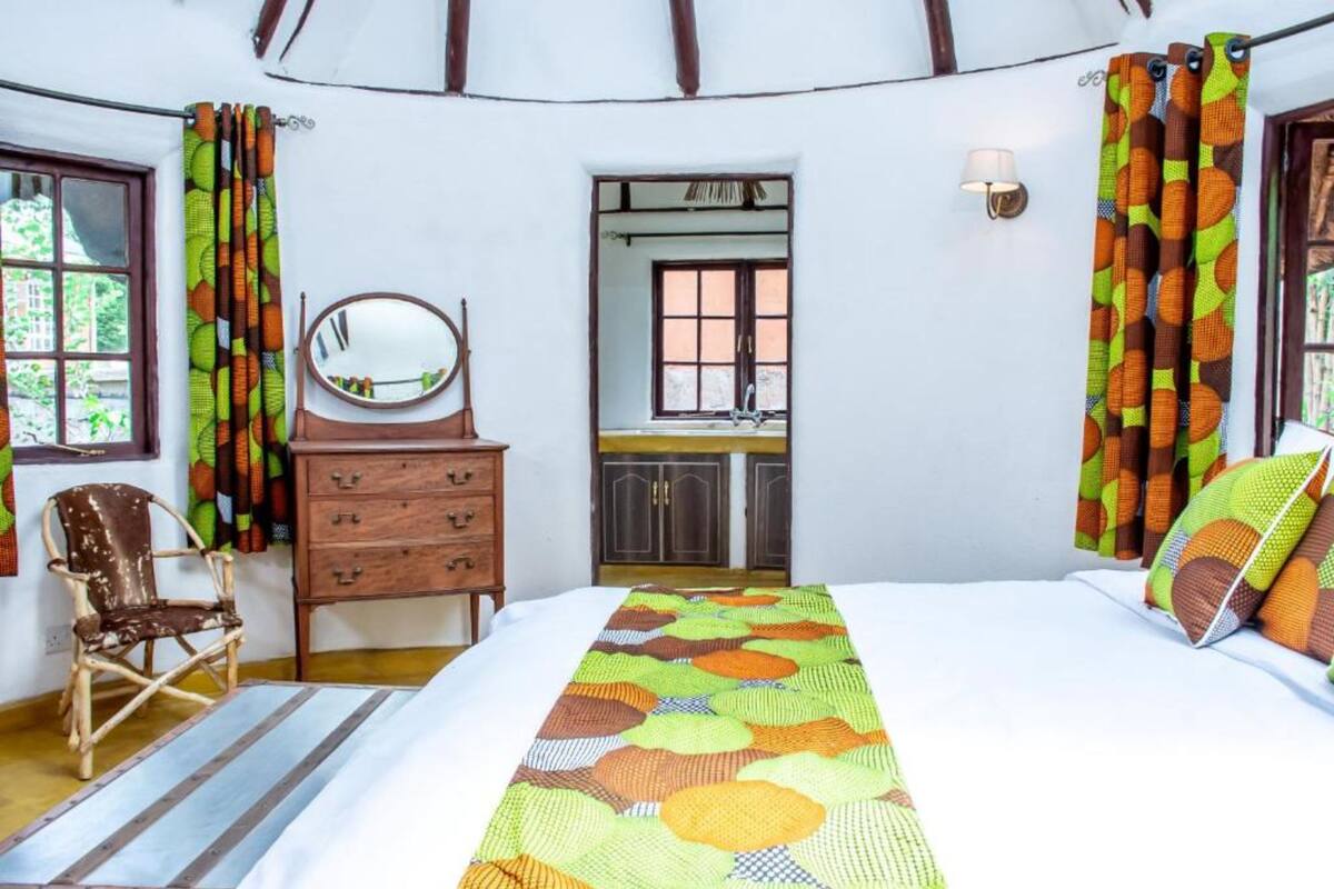 Quarto com cama, cômoda de madeira, cadeira, espelho, janela e cortinas.