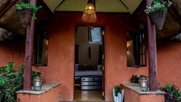 A rustic entrance with a thatched roof, a hanging light fixture, and potted plants.