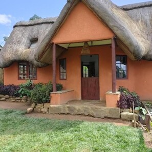 A thatched-roof house with a porch and a door. - Etana Cottage (Kakamega)