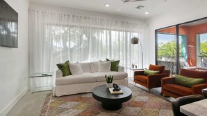 A modern living room with a white sofa, orange armchairs, a black coffee table, and a large window with sheer curtains. - The Garden District's Pied-à-Terre on Prytania | 4 Bedrooms (New Orleans)