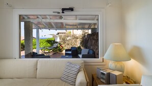 Une pièce comprenant un canapé, une lampe, un téléviseur et une fenêtre donnant sur un jardin.