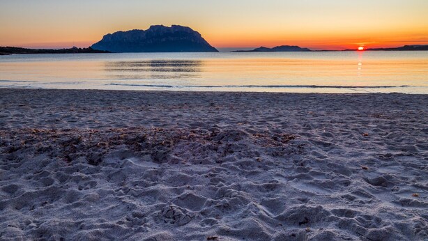 Une plage avec un promontoire rocheux à l’horizon, au coucher du soleil.