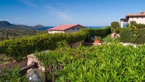 Une villa côtière avec un toit recouvert de tuiles rouges, entourée d’une végétation luxuriante et offrant une vue sur la mer.