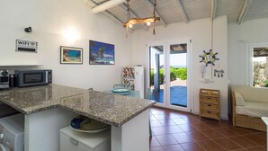 Une cuisine équipée d’un plan de travail en granit, d’un four à micro-ondes, d’un lave-linge et d’un réfrigérateur. Une porte donne accès à une terrasse avec vue sur l’océan.