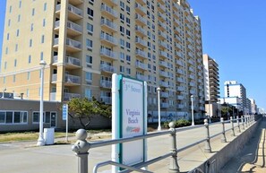 A high-rise building with balconies, a street sign for 3rd Street, and a beach sign indicating Virginia Beach.