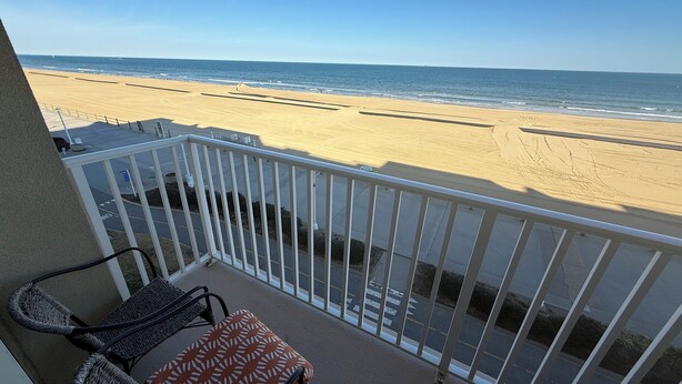 A balcony with a view of the beach, a chair, and a small table. - Dolphin Beach condo with indoor pool, ocean views, steps to the beach (Virginia Beach)