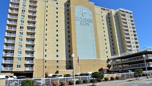 A high-rise hotel with a prominent 'Dolphin Run' sign, multiple balconies, and a parking area in front. - Dolphin Beach condo with indoor pool, ocean views, steps to the beach (Virginia Beach)