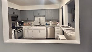 Una cocina compacta con armarios grises, lavavajillas de acero inoxidable y microondas.