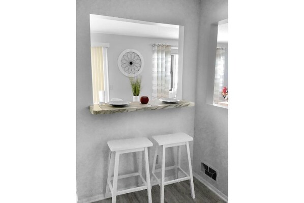 A modern bathroom with a large mirror, white stools, a marble countertop, and a potted plant.