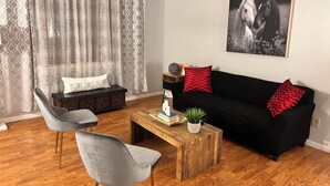Una sala de estar con un sofá negro, dos sillones grises, una mesa de centro de madera y una cortina estampada.
