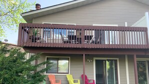 Una casa de dos pisos con balcón, un porche cubierto y sillas Adirondack de colores.