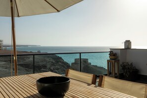 Een balkon met uitzicht op zee, een houten tafel en een zwarte schaal.