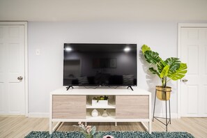 Una sala de estar moderna con un televisor de pantalla plana sobre un mueble blanco de madera, una planta en maceta y un jarrón decorativo.