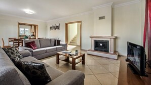 A living room with a sofa, coffee table, fireplace, TV, and a staircase leading to another room. - Villa Das Oliveiras, Large grounds, walk to Marina (Albufeira)
