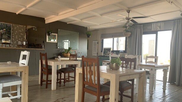 A dining area with wooden tables and chairs, a ceiling fan, and a large window with curtains. - Three Thymes Inn (Pretoria)