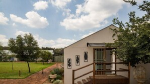 A building with a wooden staircase leading to a covered porch, surrounded by a landscaped garden with a brick pathway. - Three Thymes Inn (Pretoria)