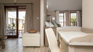 A room with a bed, a bedside table, a chair, a bench, and a window with curtains. - Three Thymes Inn (Pretoria)