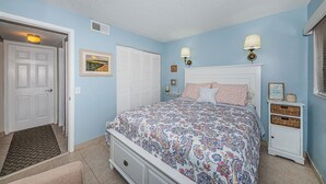 Ein Schlafzimmer mit einem Bett, Nachttischen, einem Fenster mit Jalousien und einer Wandleuchte.